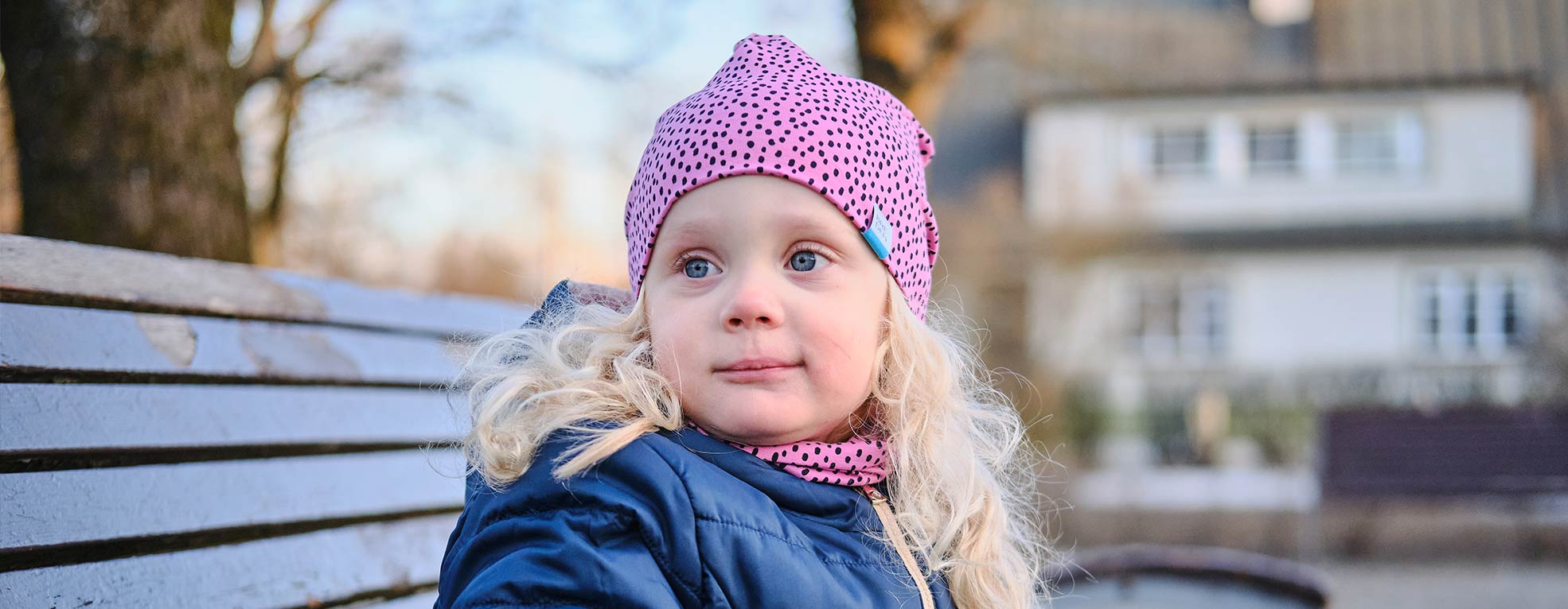 girl sitting on a bench in a pink dotted organic cotton hat and scarf